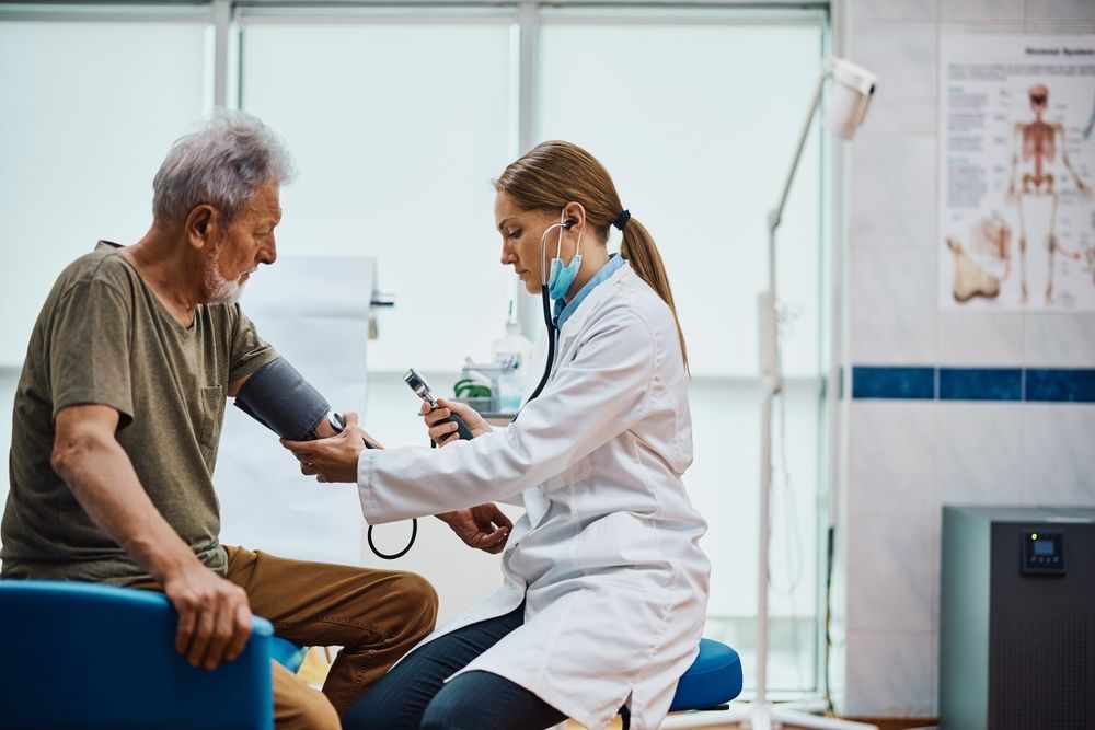 Doctor taking a patient's blood pressure with stethoscope and cuff in a medical office.