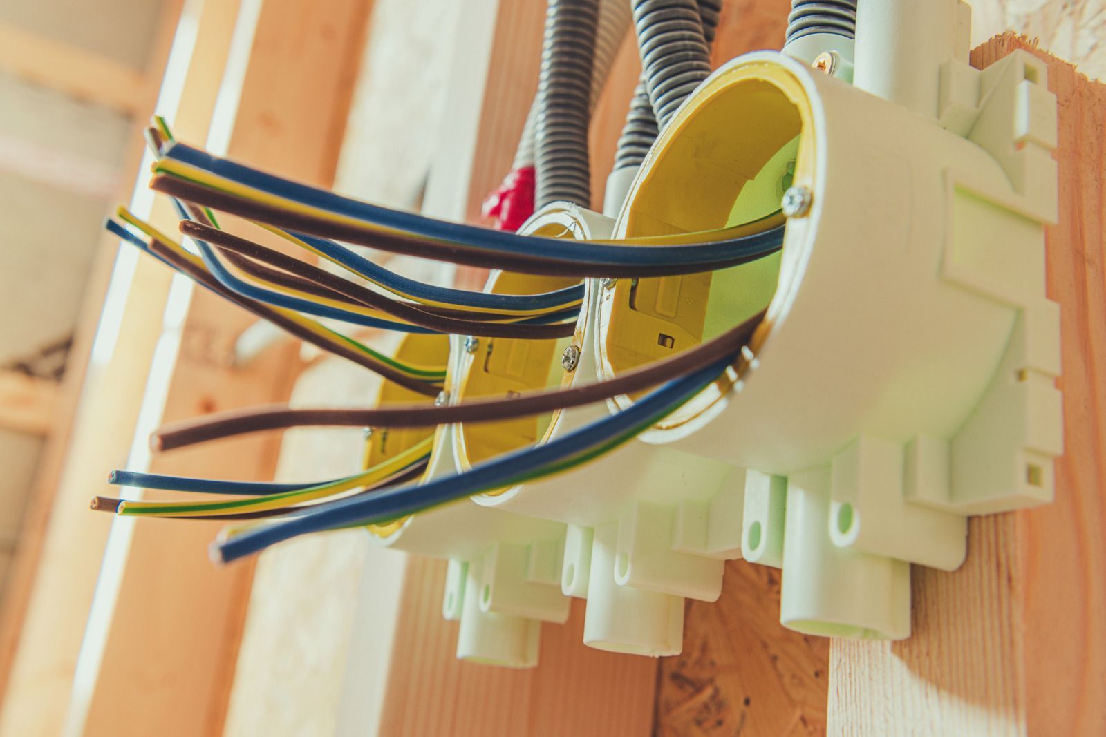 A bunch of wires are coming out of electrical boxes on a wall.