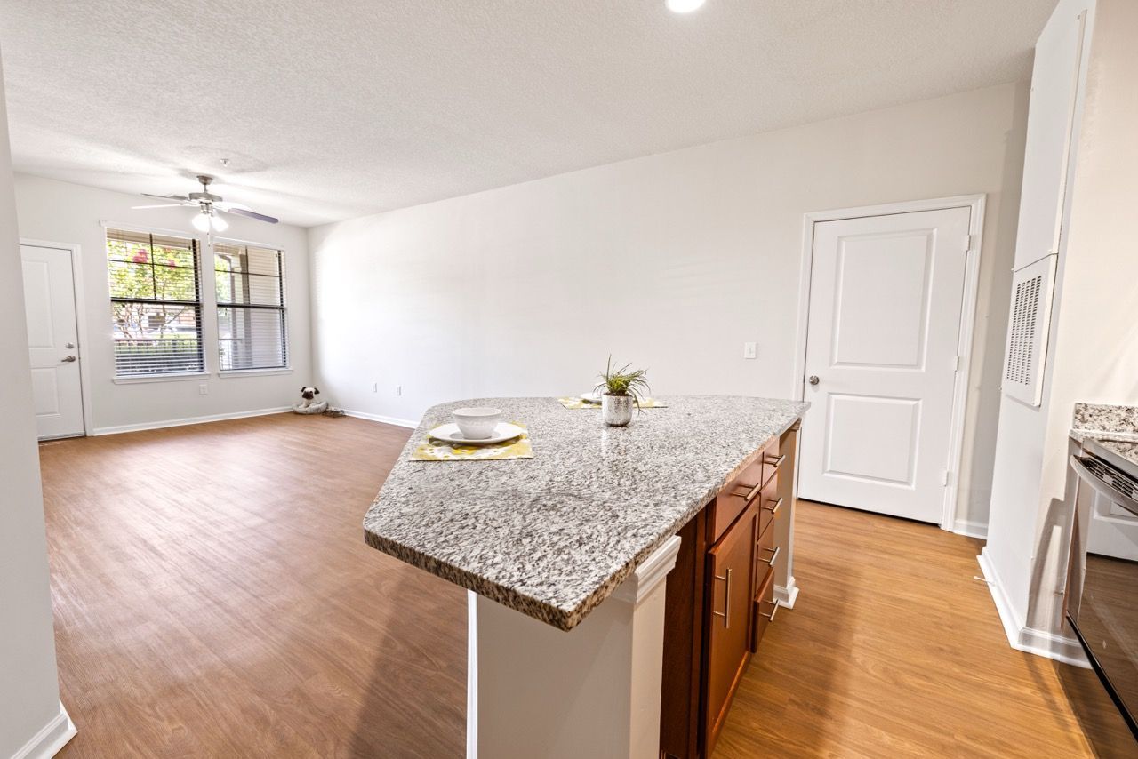 Open-concept kitchen with granite island, hardwood floors, and a living area with large windows.