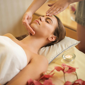 Woman receiving facial massage in a spa setting with lit candle and flowers.