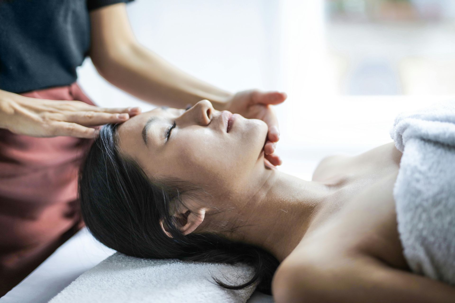 Woman receiving a facial massage at spa; therapist's hands on her head.