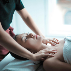 Person receiving a massage on a spa bed, another person massaging their shoulders.