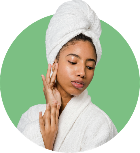 Woman in a towel and robe, touching her face, with a green background.
