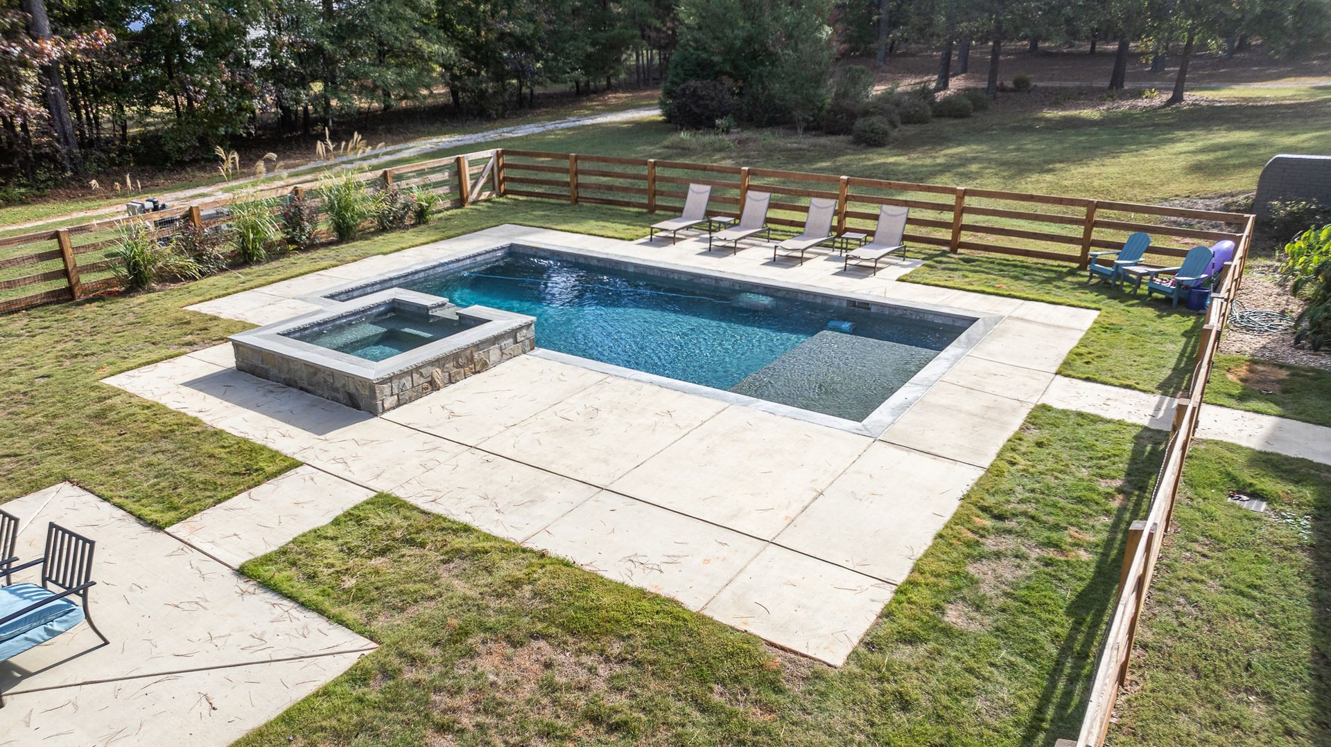 An aerial view of a large swimming pool with a hot tub in the backyard.
