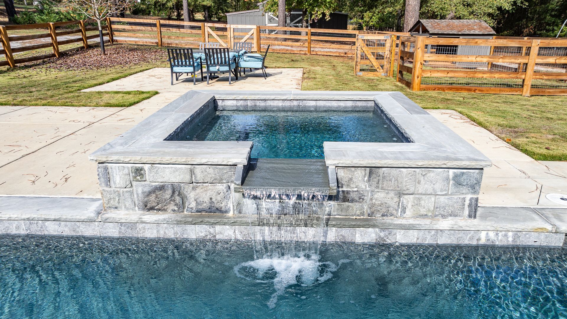 A swimming pool with a hot tub and a wooden fence in the background.