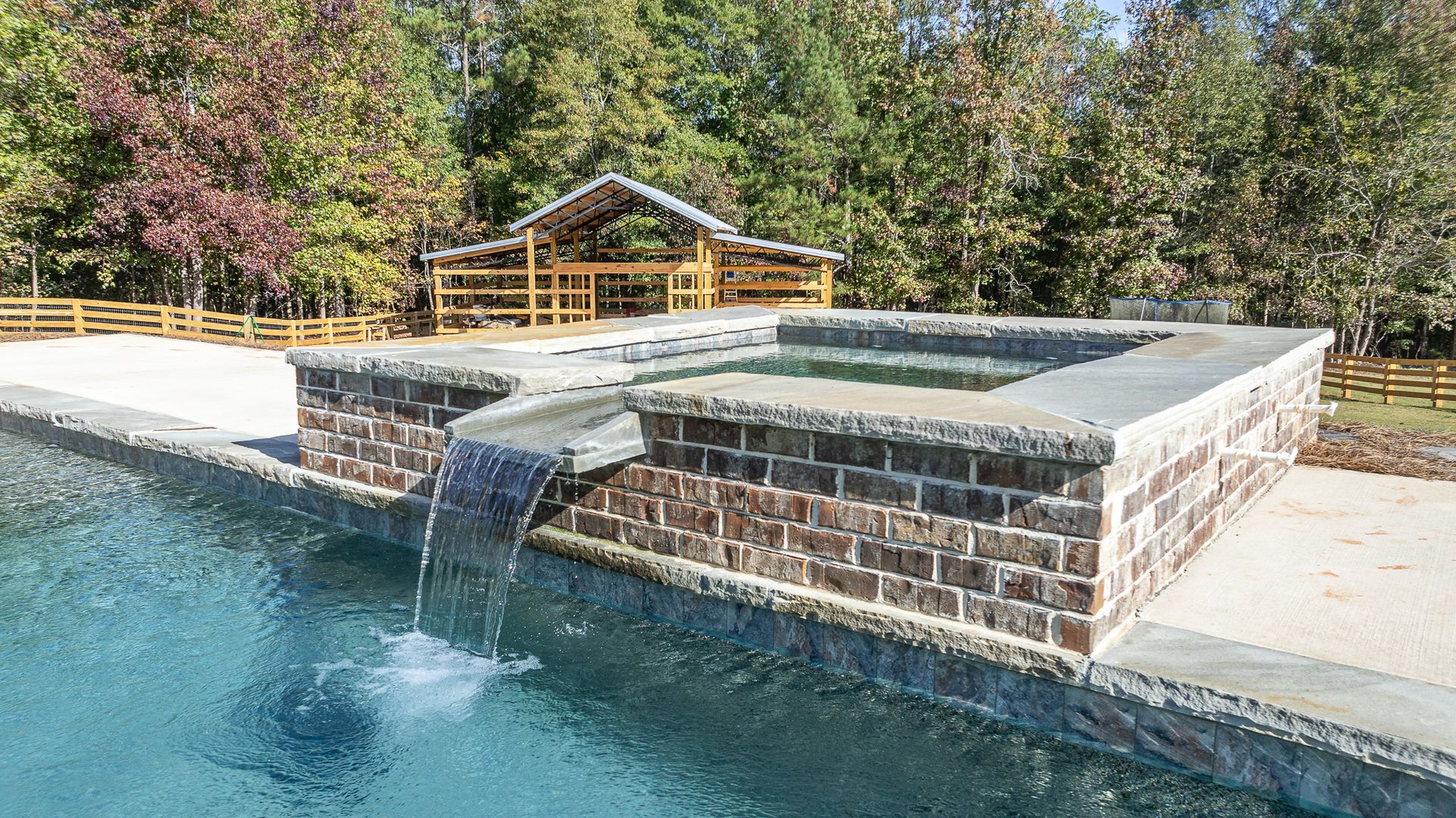 A swimming pool with a waterfall and a gazebo in the background.