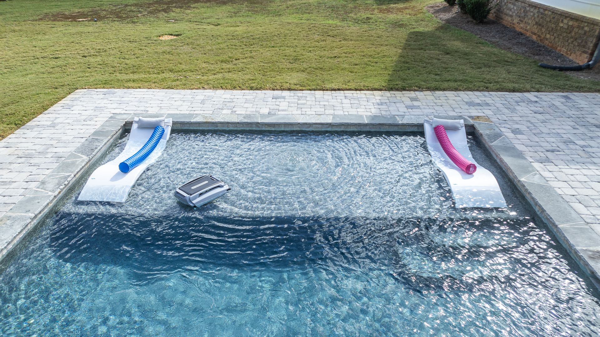 A swimming pool with two lounge chairs in the water.
