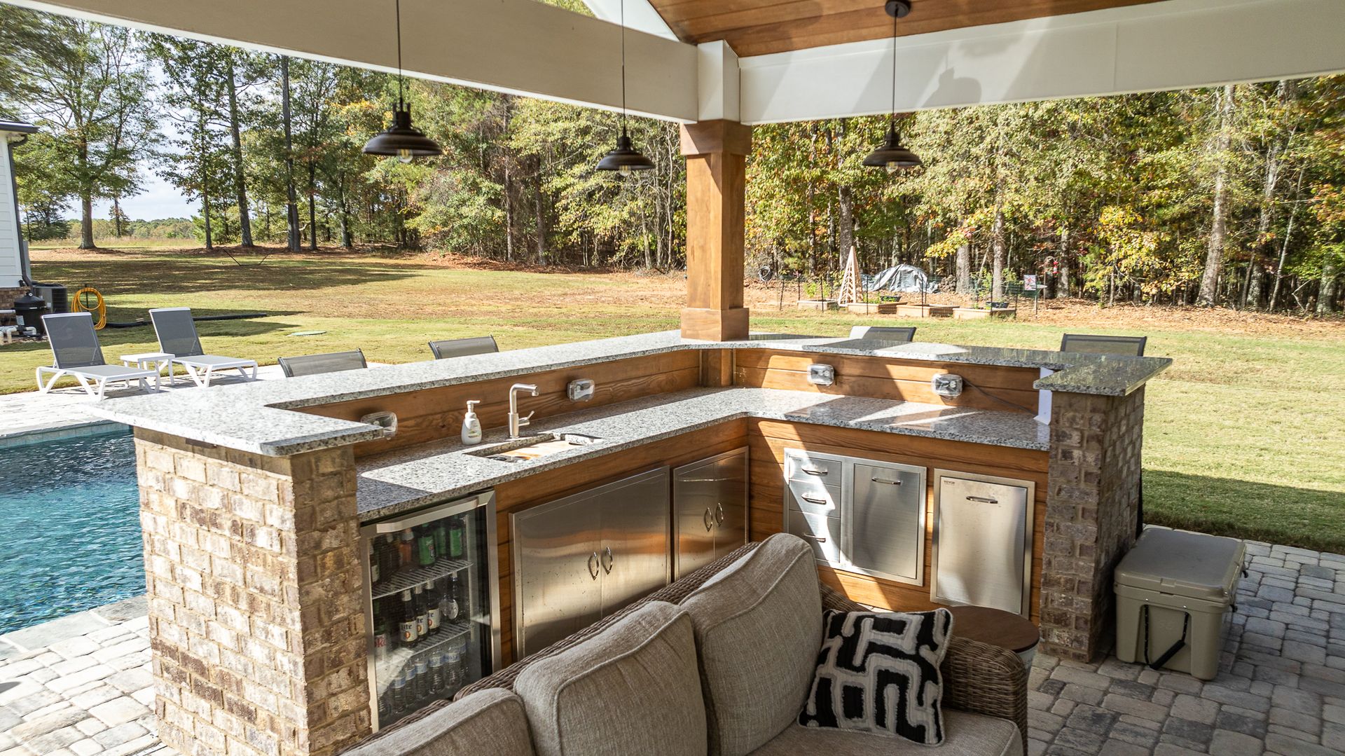 A large outdoor kitchen with a couch and a pool in the background.