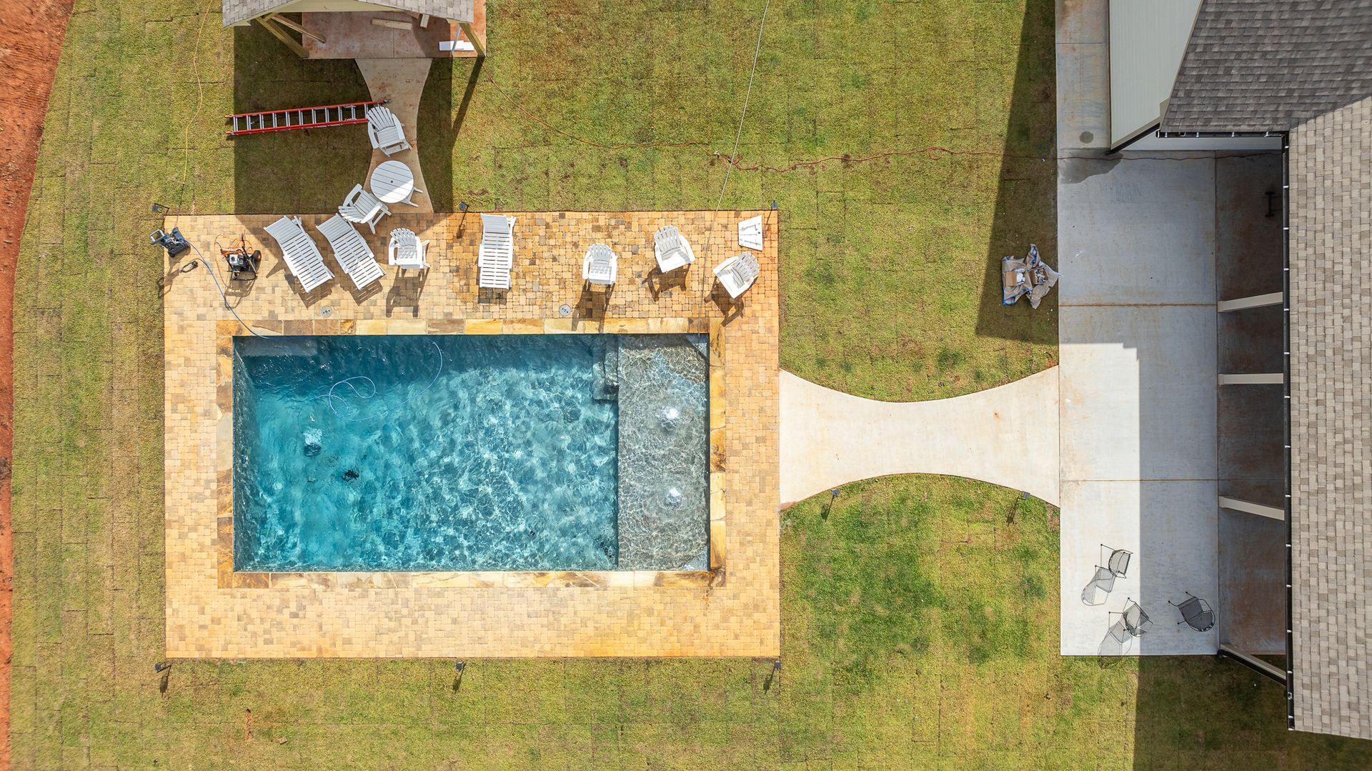 An aerial view of a swimming pool surrounded by chairs and a house.