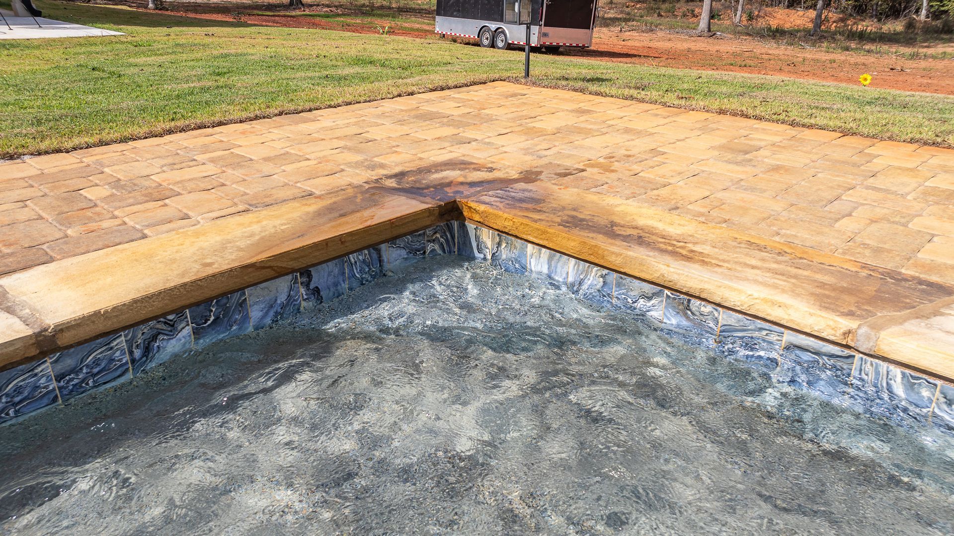 A swimming pool is surrounded by grass and a brick walkway.