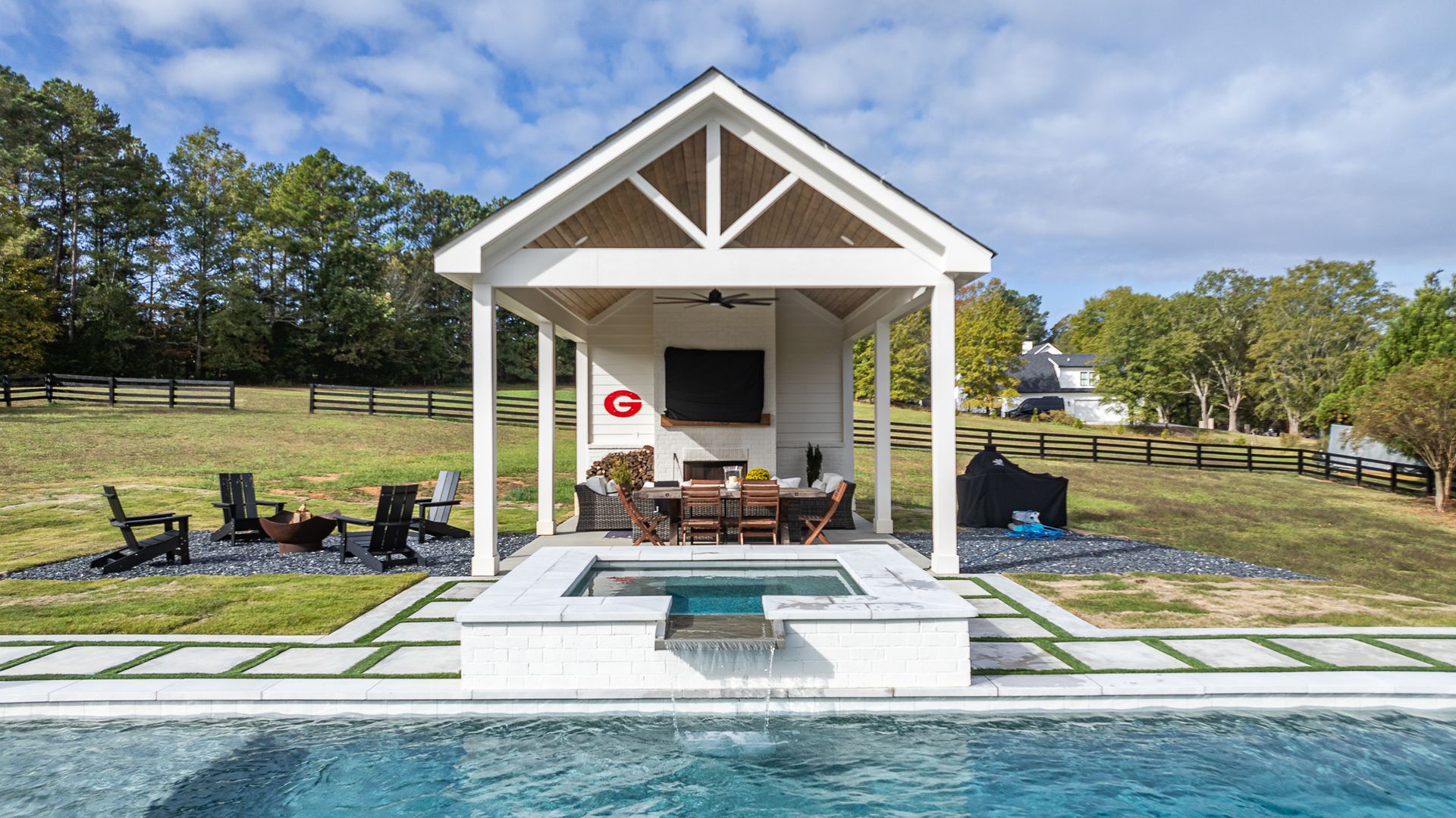 There is a pool with a gazebo and a table and chairs in front of it.