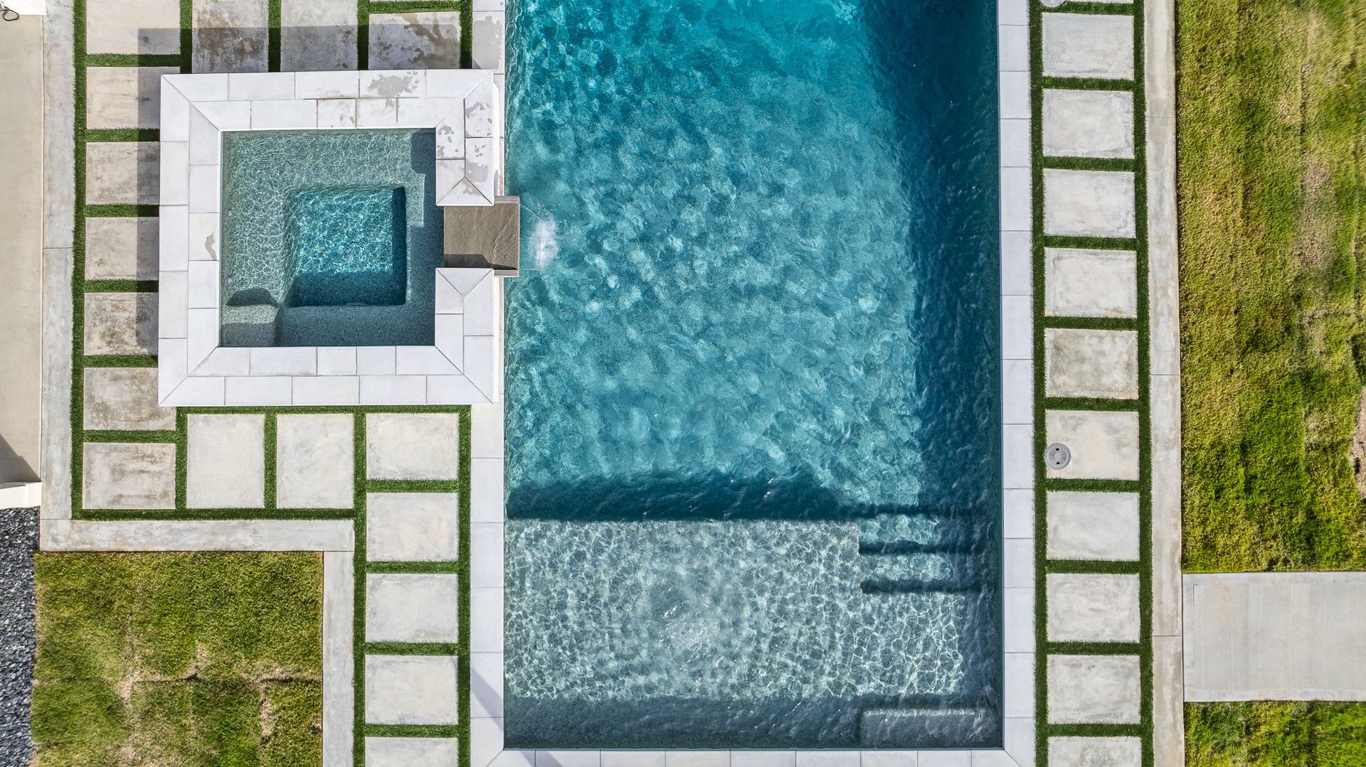 An aerial view of a large swimming pool with a hot tub in the backyard.