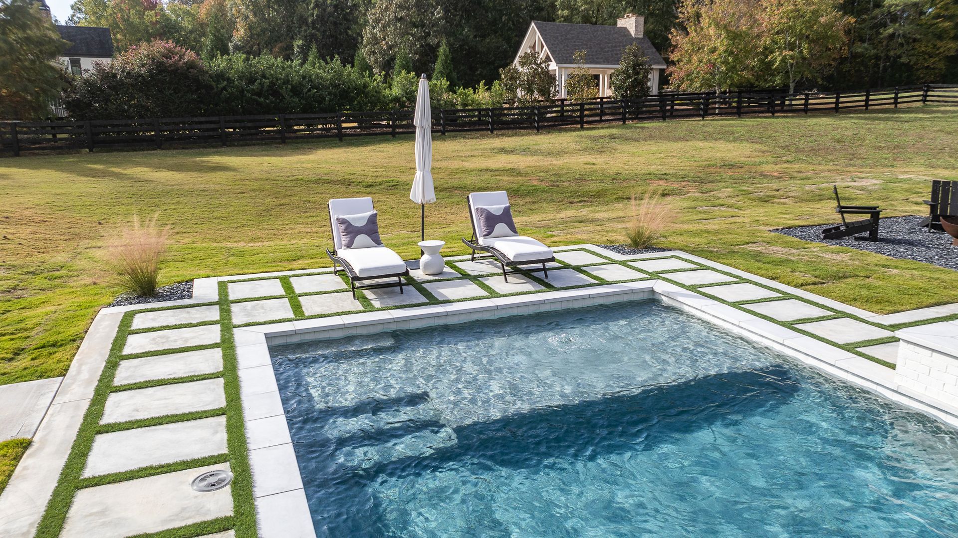 A large swimming pool with two lounge chairs and an umbrella in the backyard.