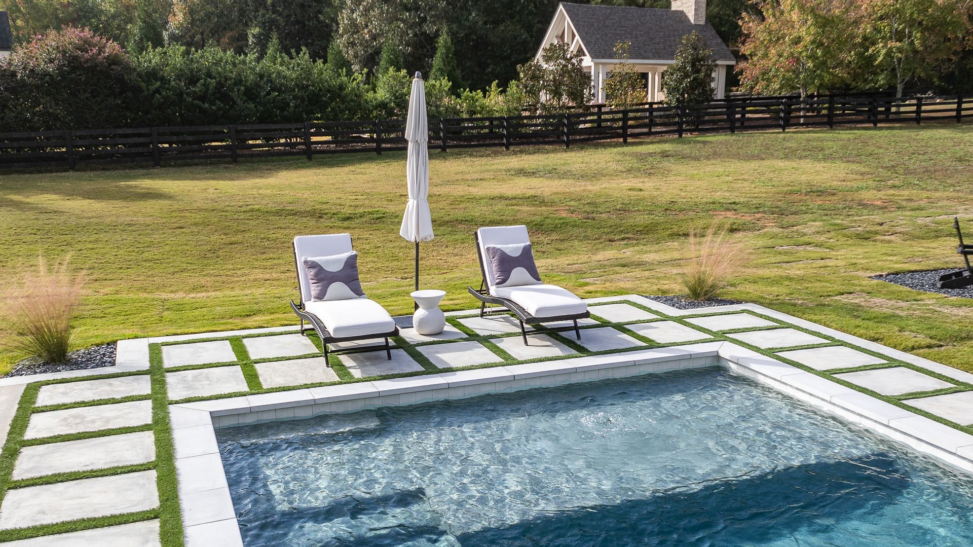 A large swimming pool surrounded by lawn chairs and umbrellas in a backyard.