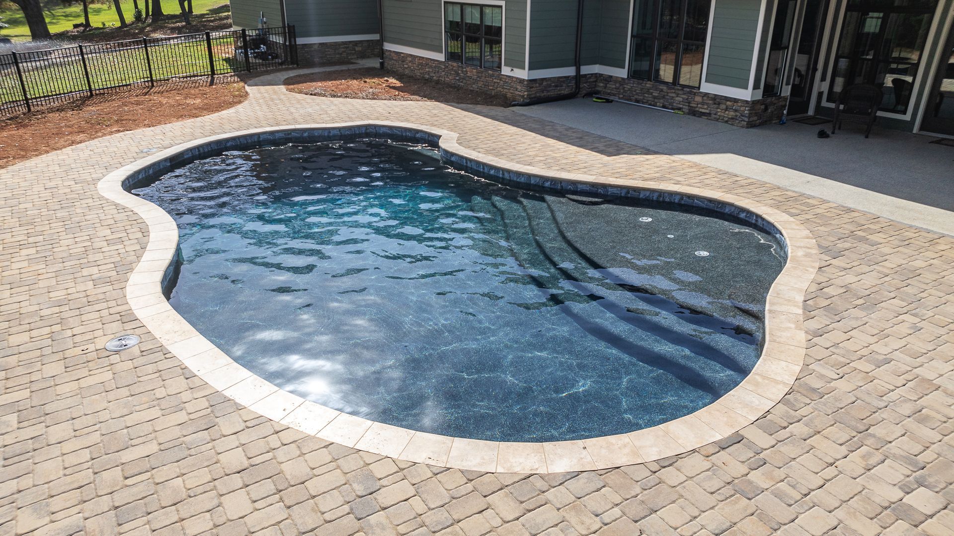 A large swimming pool is sitting on a brick patio in front of a house.