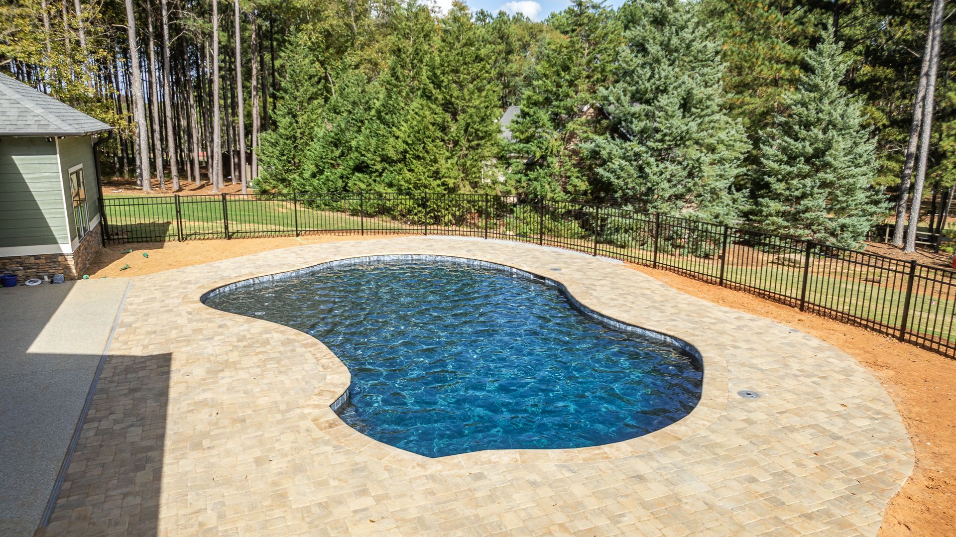 A large swimming pool in the backyard of a house surrounded by trees.
