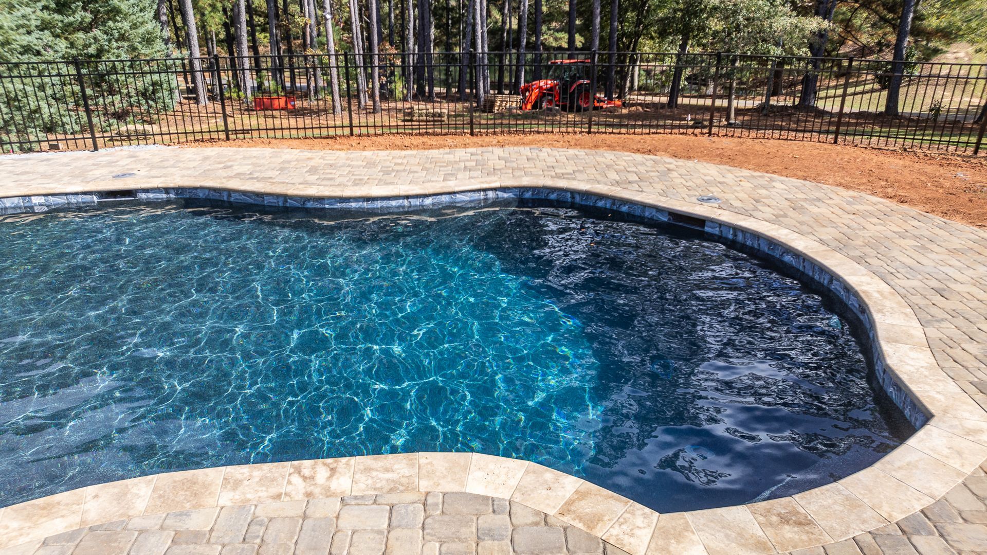 A large swimming pool surrounded by a brick patio and a fence.