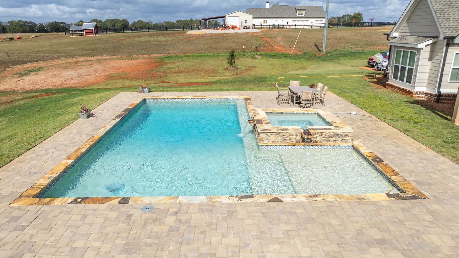A large swimming pool with a patio in front of a house.