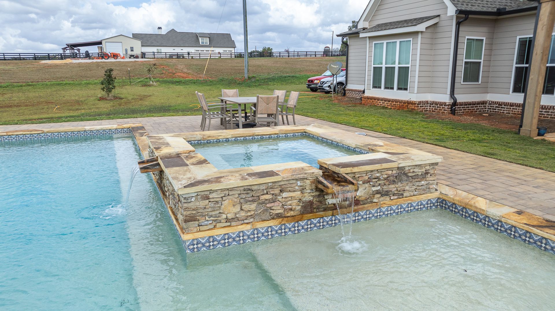 A large swimming pool with a hot tub in the middle of it in front of a house.