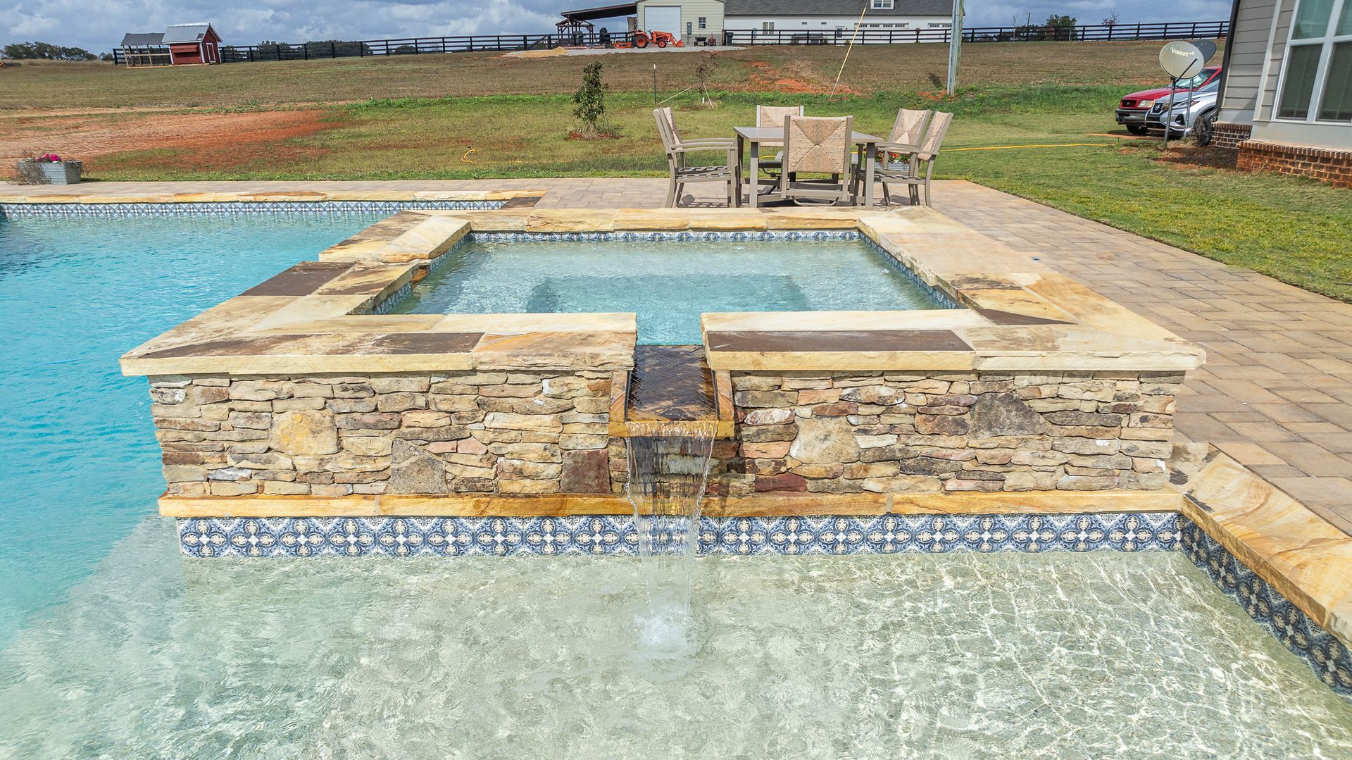 A swimming pool with a hot tub and a table and chairs in the background.