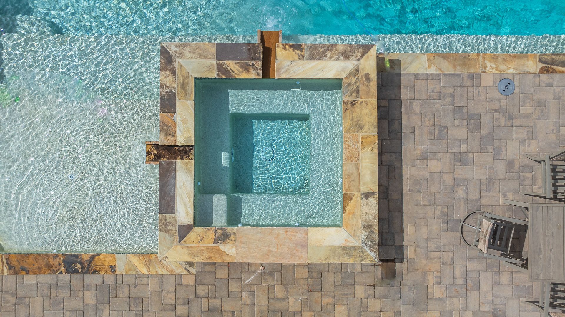 An aerial view of a square hot tub next to a swimming pool.