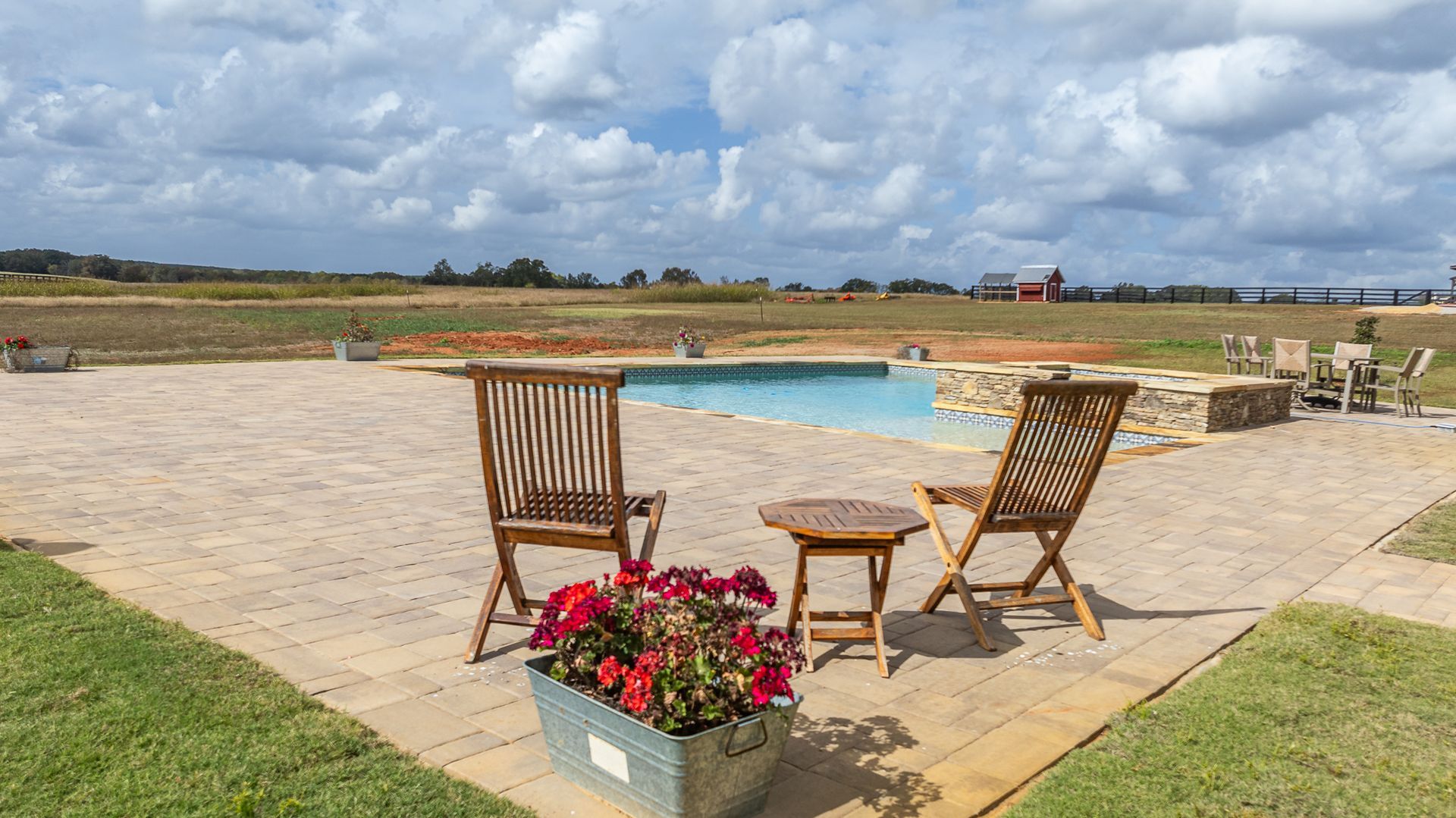 A patio with chairs and a table next to a swimming pool.