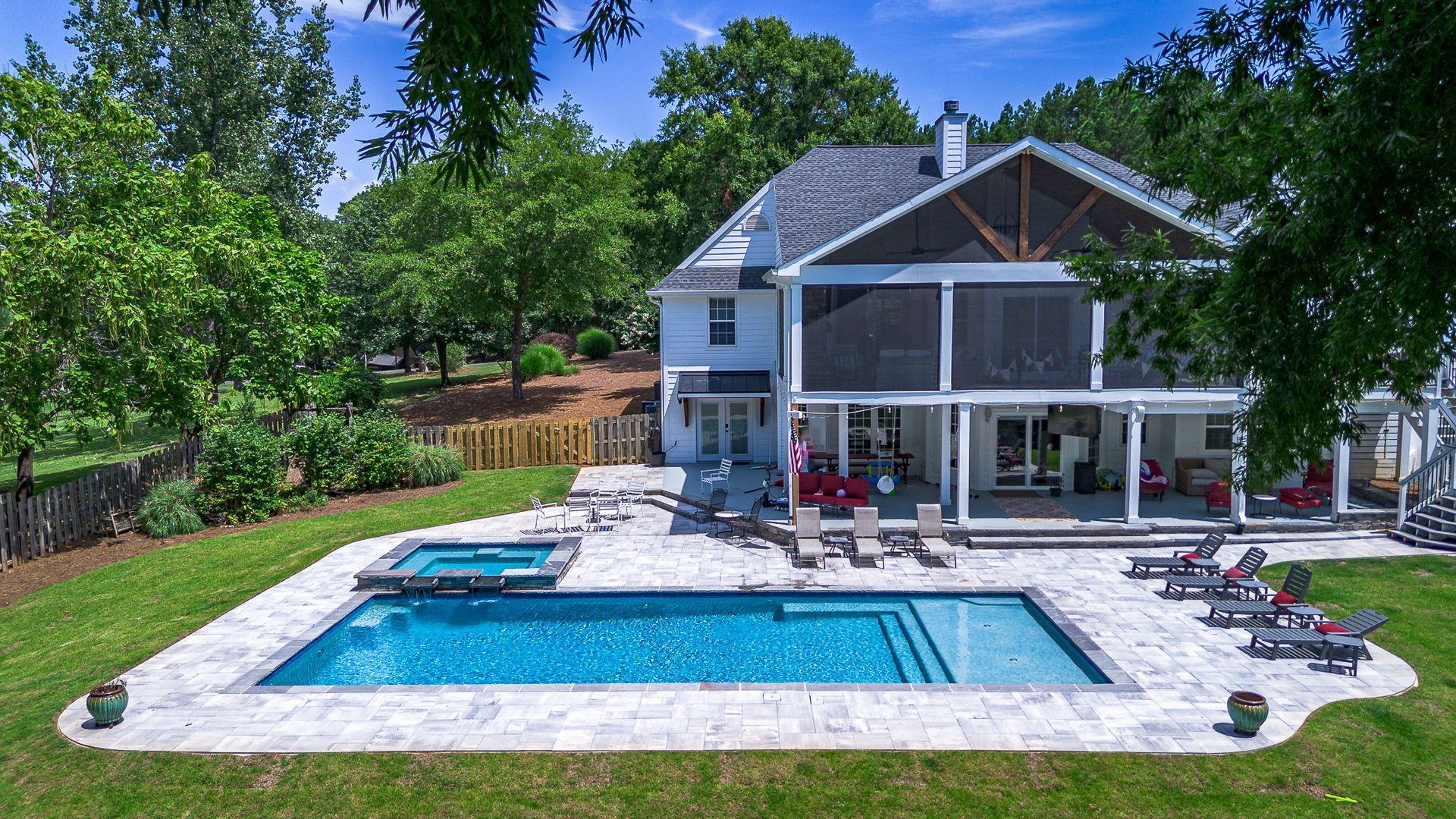 White house with pool and hot tub in backyard, surrounded by green grass and trees.