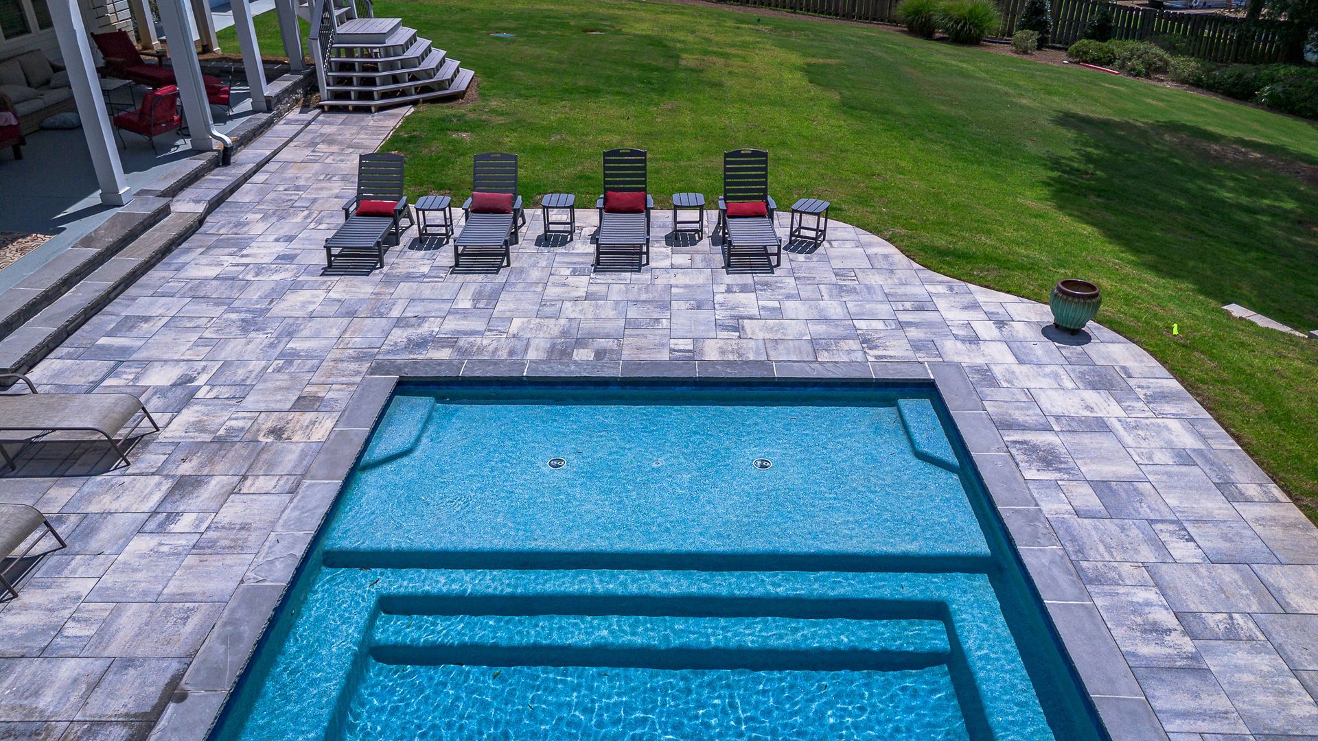 Swimming pool surrounded by gray pavers, with lounge chairs and a green lawn.