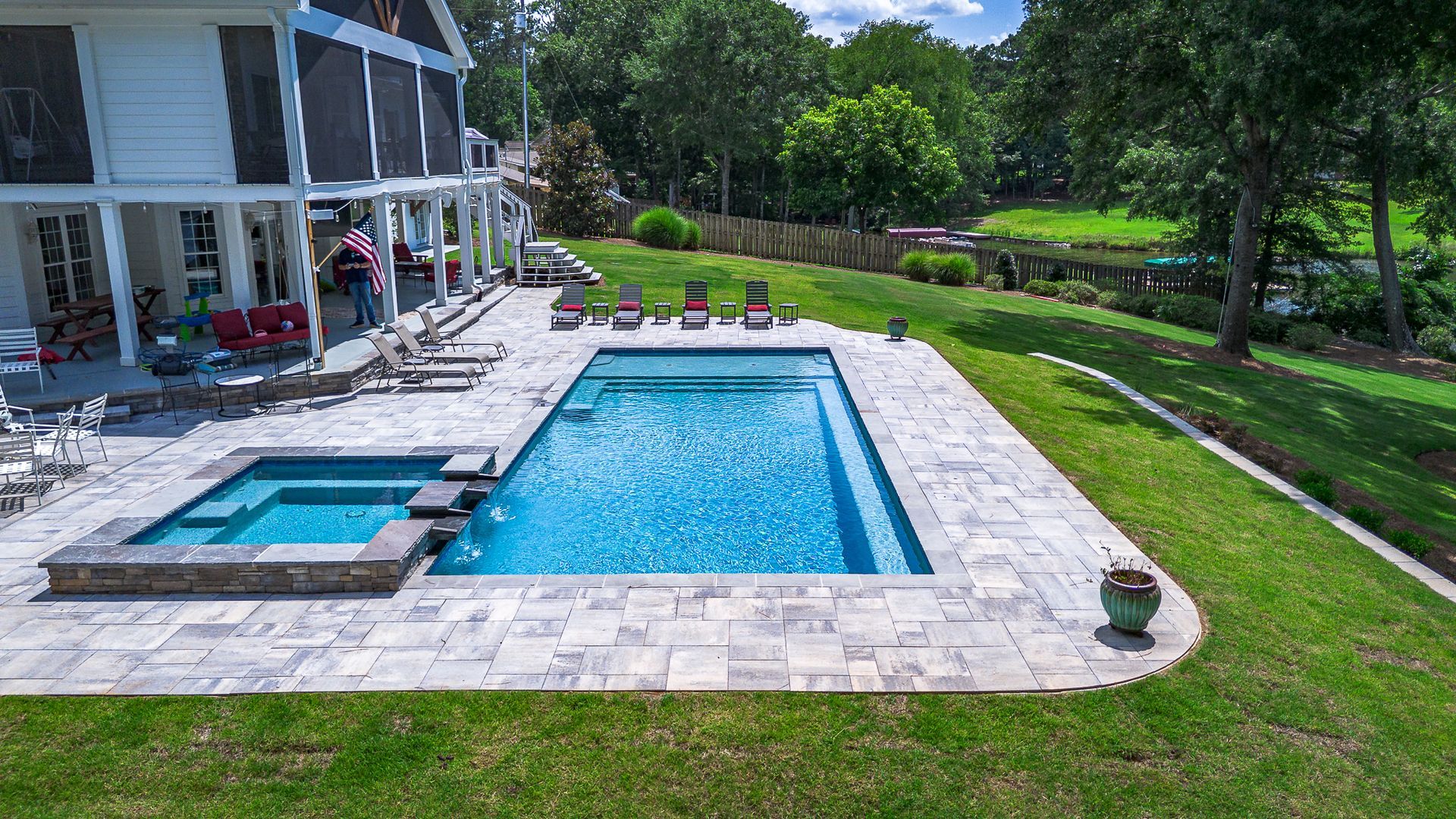 Backyard with a pool and spa next to a house on a sunny day.