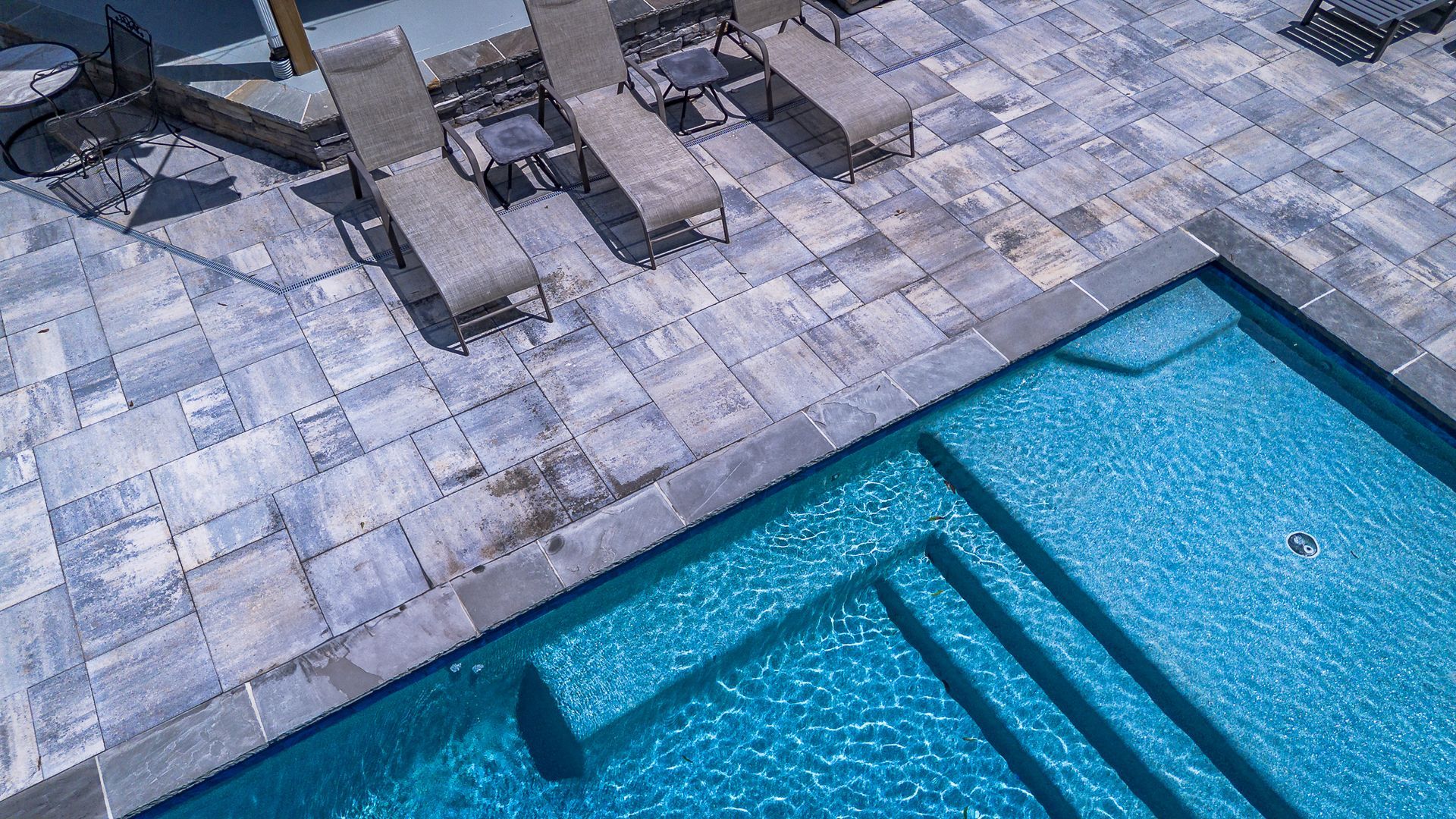 Pool with blue water, stone patio with lounge chairs.