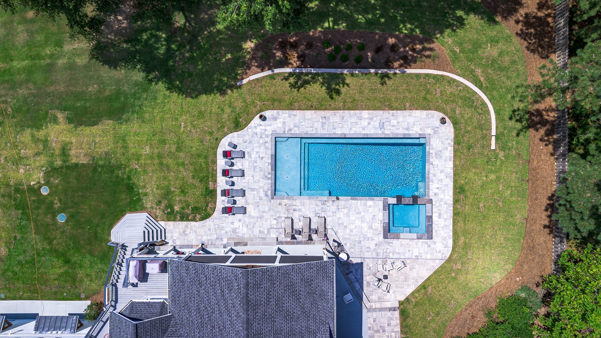 Overhead view of a house with a blue pool, a stone patio, and green lawn.