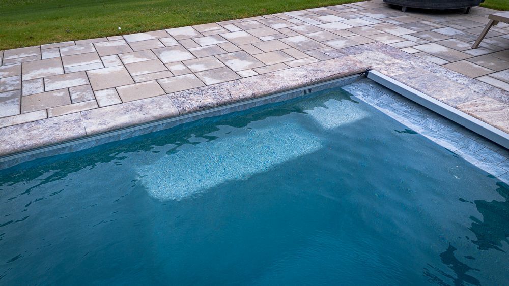 Pool with in-pool steps, edged with grey paving stones, and a green lawn nearby.