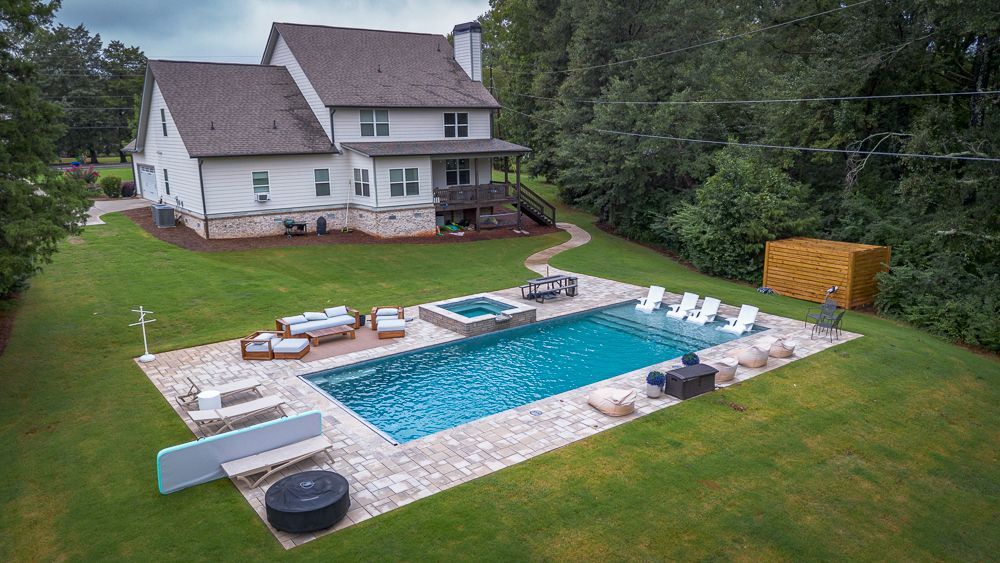Large house with backyard pool, patio seating, and green lawn.