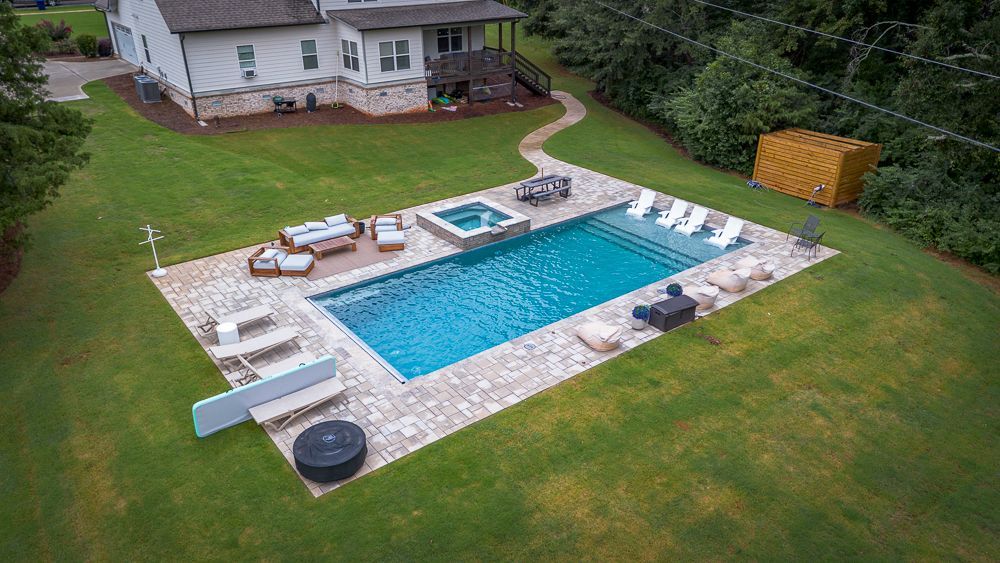 Aerial view: Pool with patio and lounge seating, house in background. Green lawn surrounds.