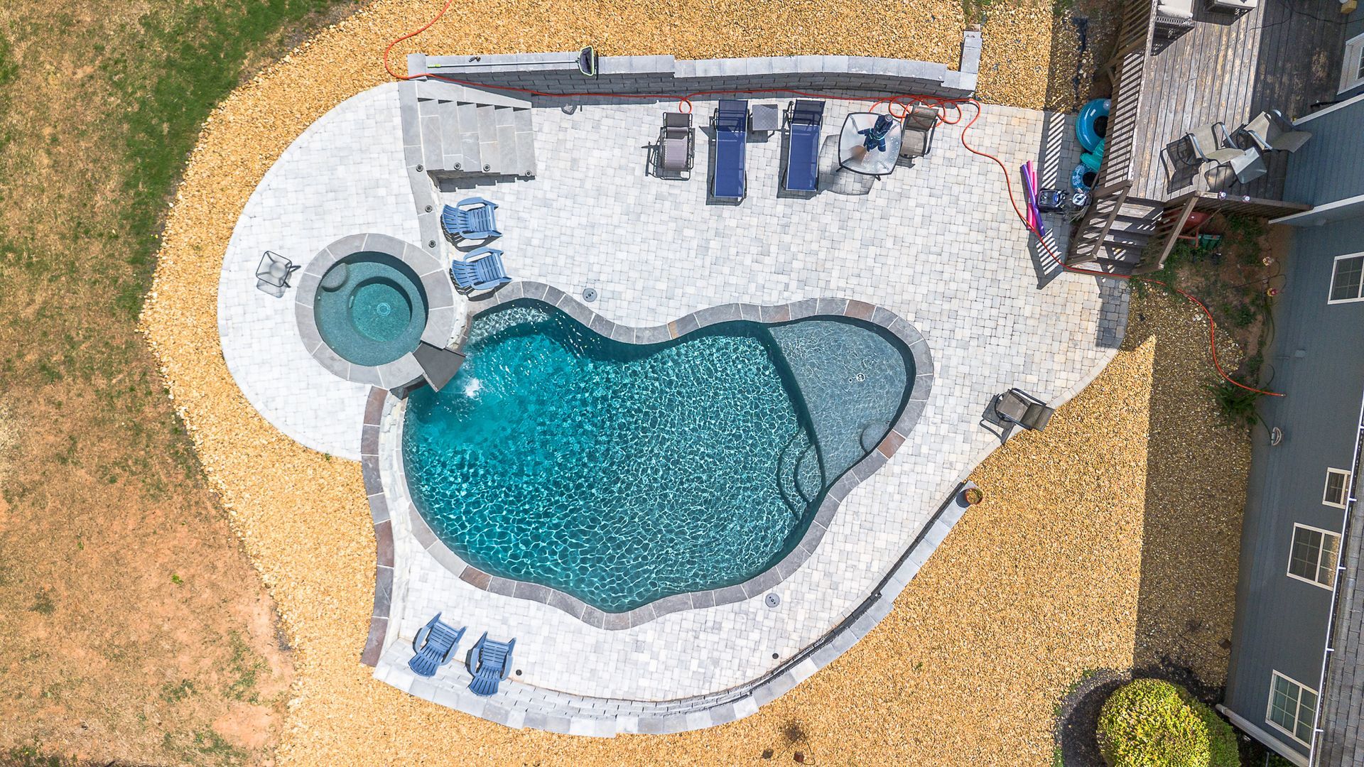 A large swimming pool is surrounded by a brick patio.