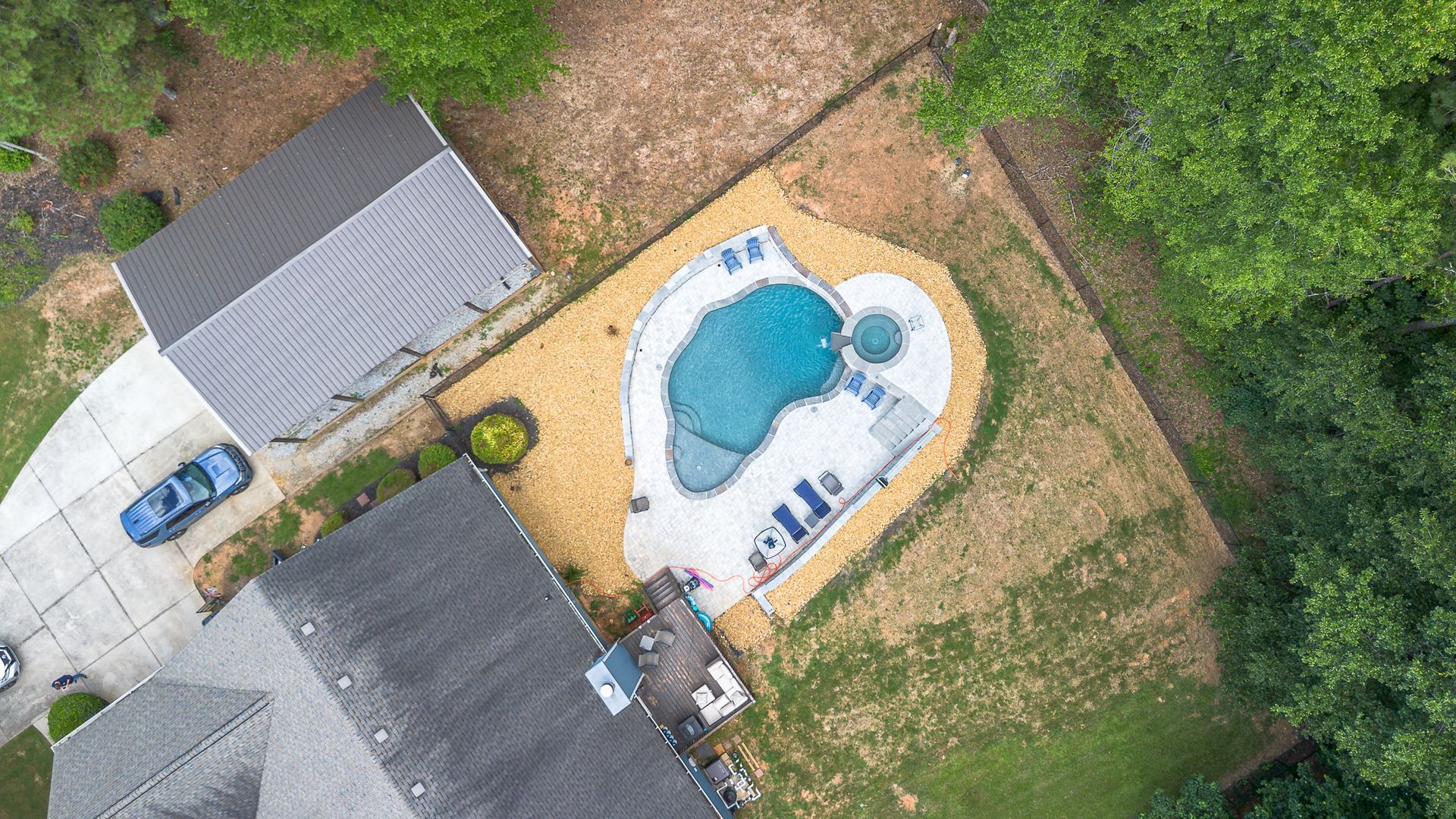 Aerial view of a backyard with a pool, patio, and a garage. A car is parked on the driveway.