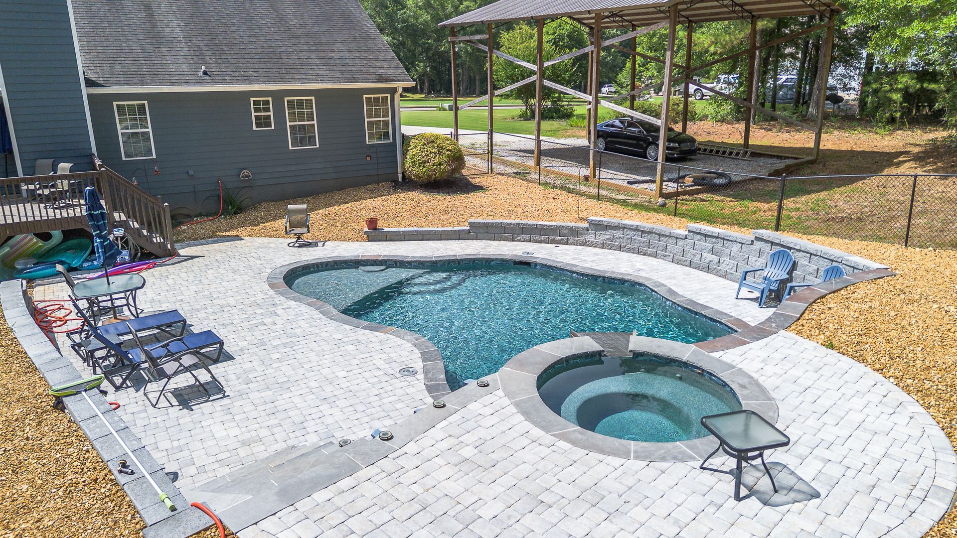 Backyard pool with paver patio, spa, and a gray house in the background.