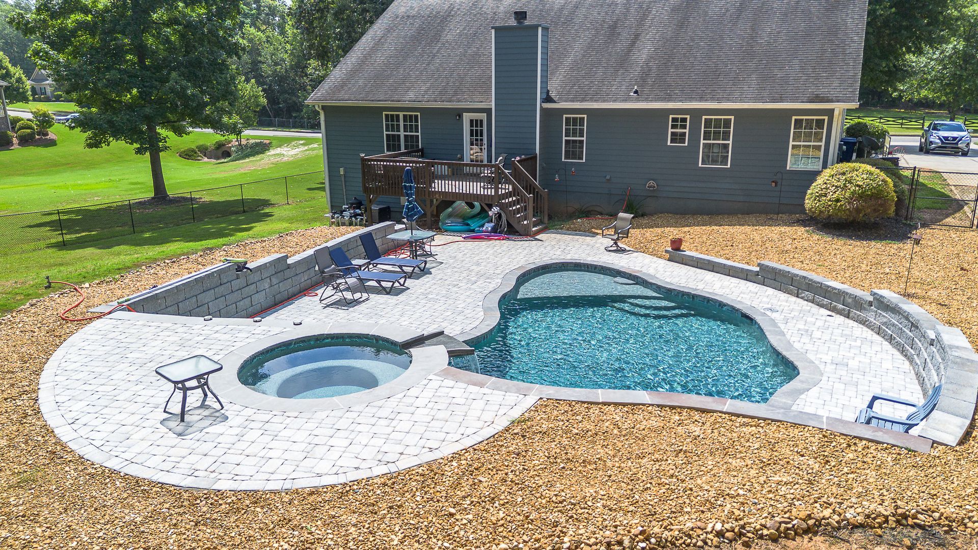 Backyard pool with hot tub, house in background; pool deck and retaining walls.
