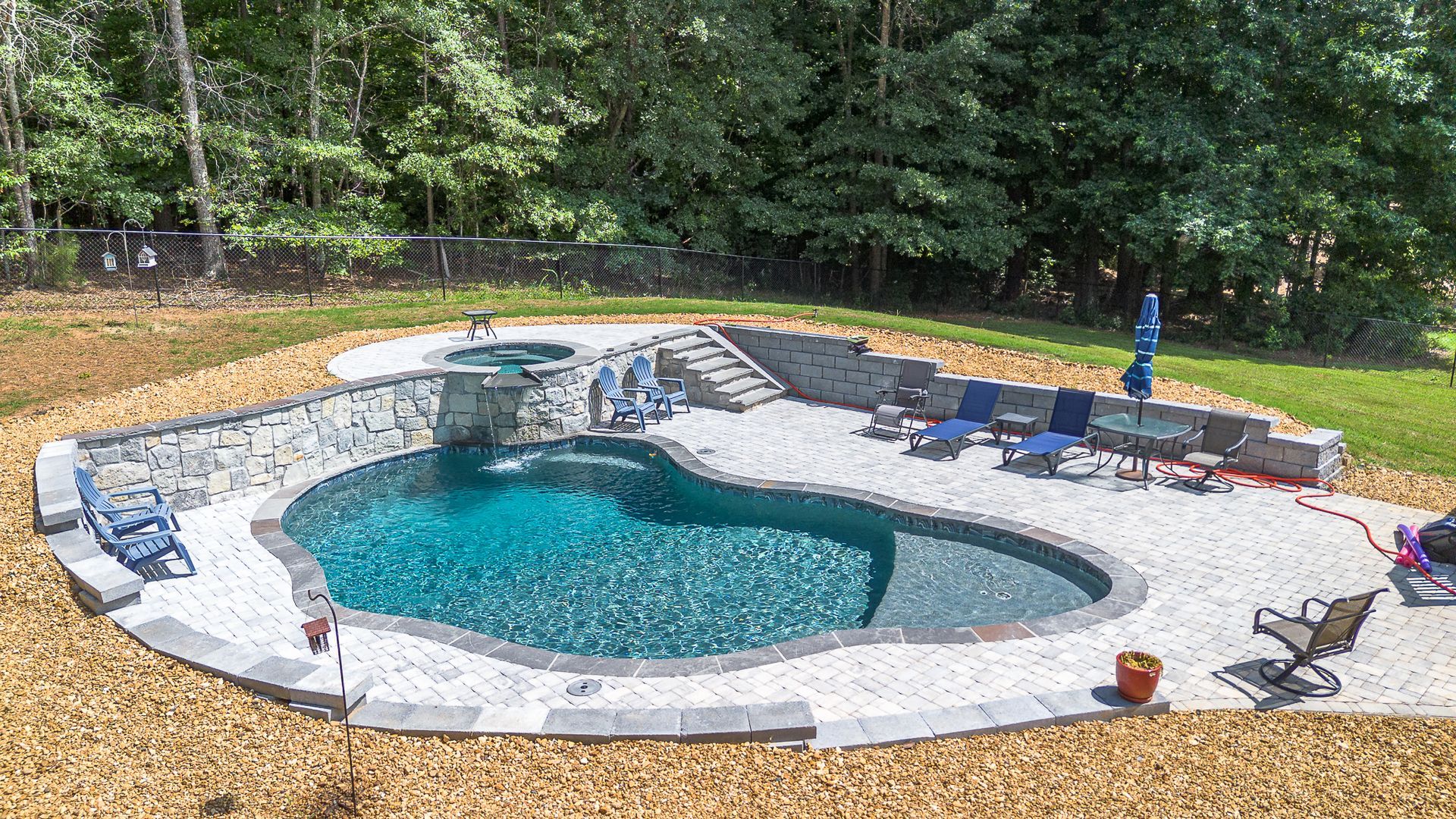 Backyard pool with blue water, waterfall, stone patio, lounge chairs, and a jacuzzi.