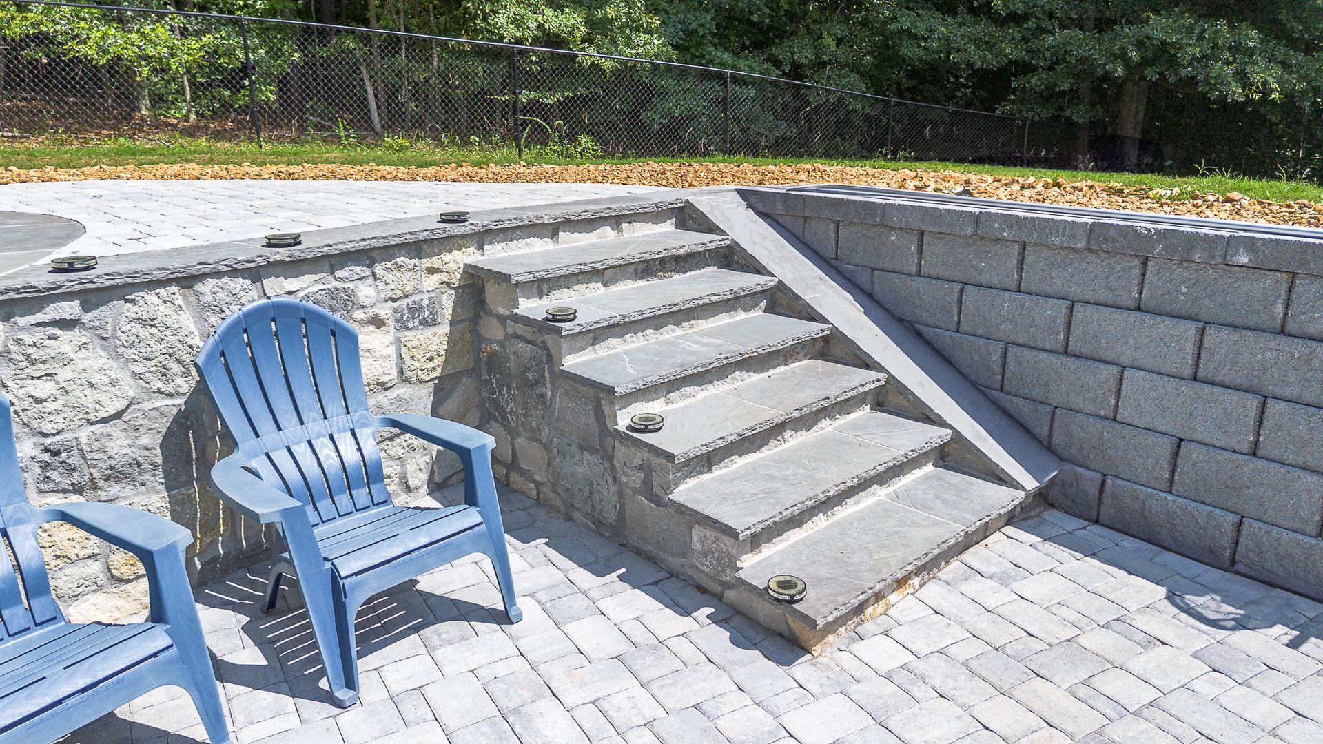 Blue chairs next to stone stairs leading up a raised patio area, gray blocks and pavers.