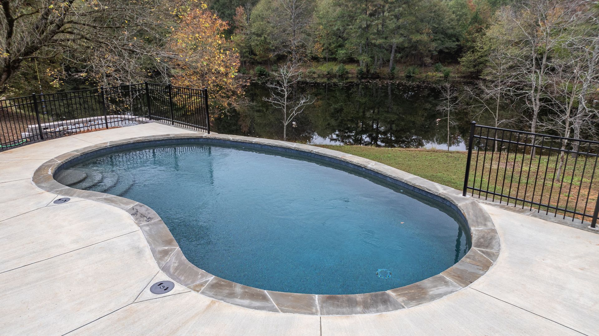 A large swimming pool is surrounded by a fence and trees.
