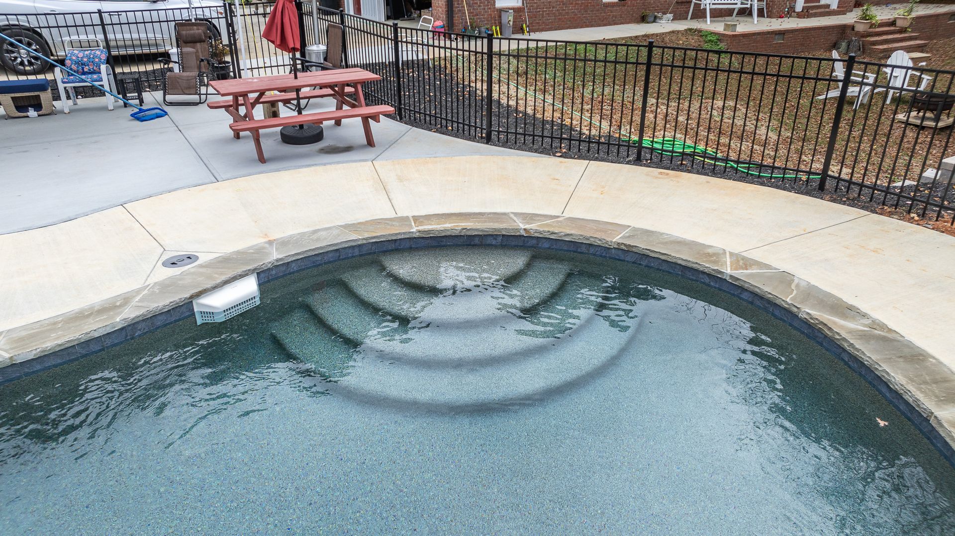 A swimming pool with stairs and a picnic table in the background.