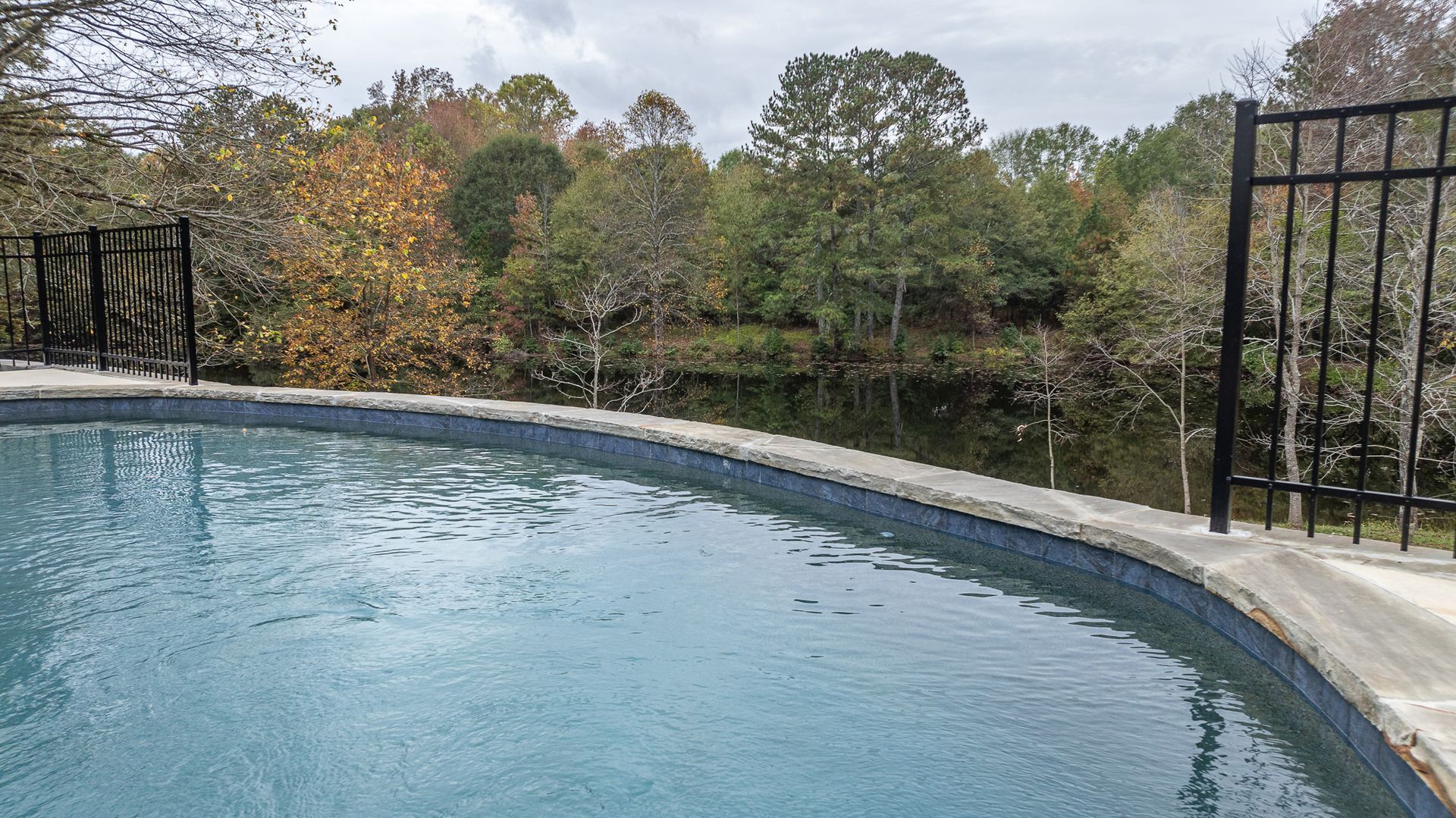 A large swimming pool with a fence around it and trees in the background.