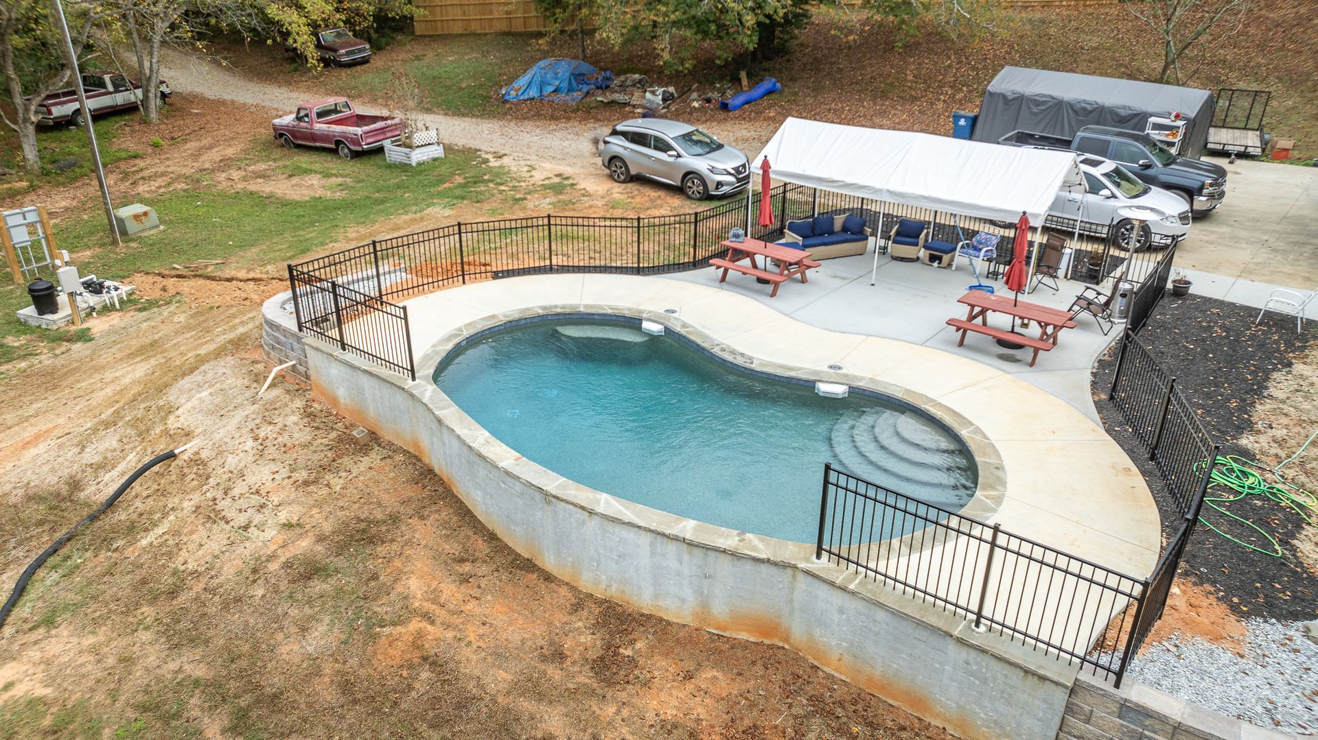 An aerial view of a large swimming pool surrounded by picnic tables and cars.