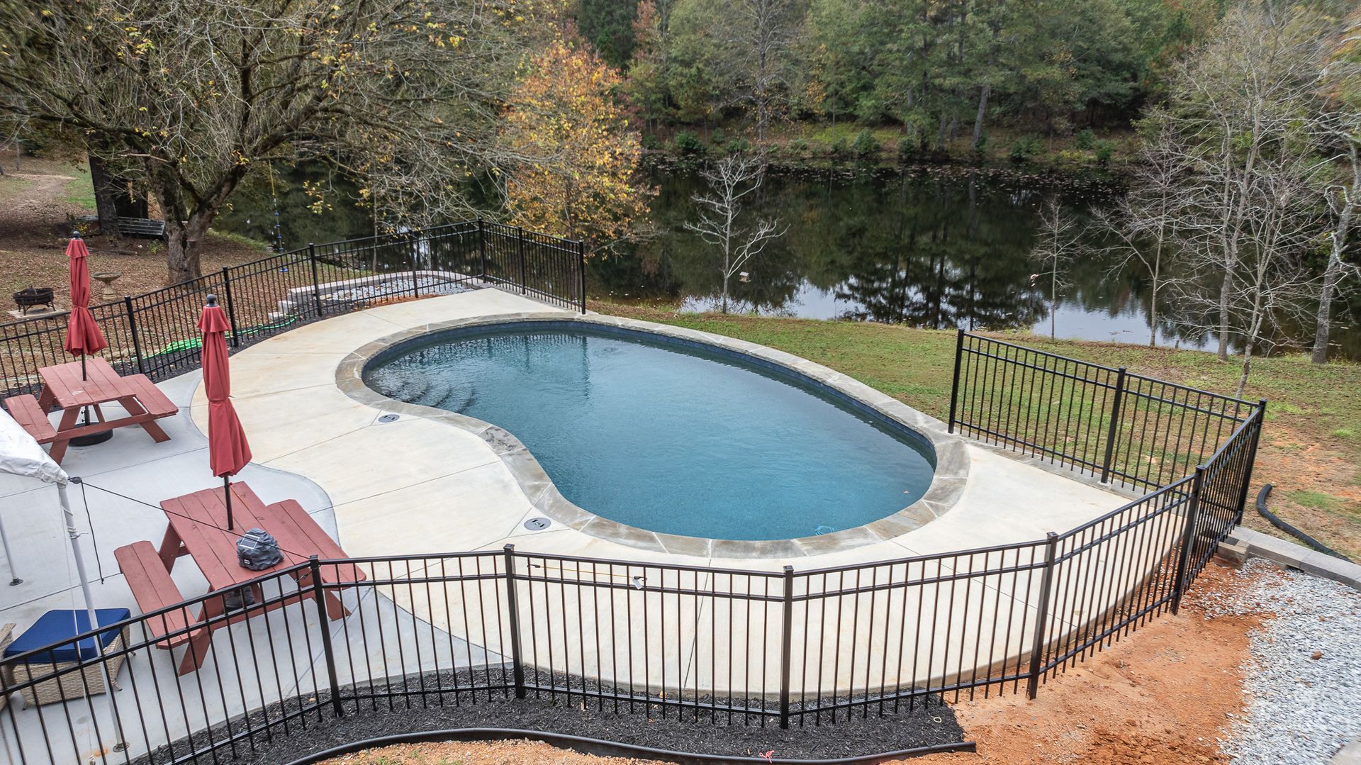 A large swimming pool surrounded by a fence and a picnic table.