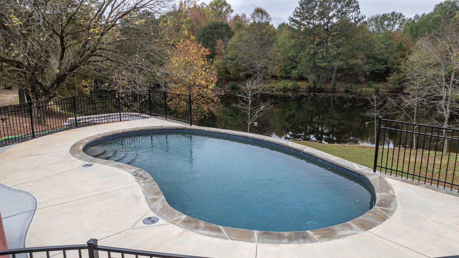 A large swimming pool is surrounded by a fence and trees.