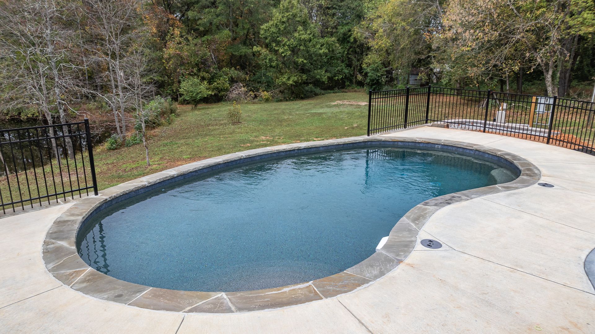 A large swimming pool is surrounded by a fence in a backyard.