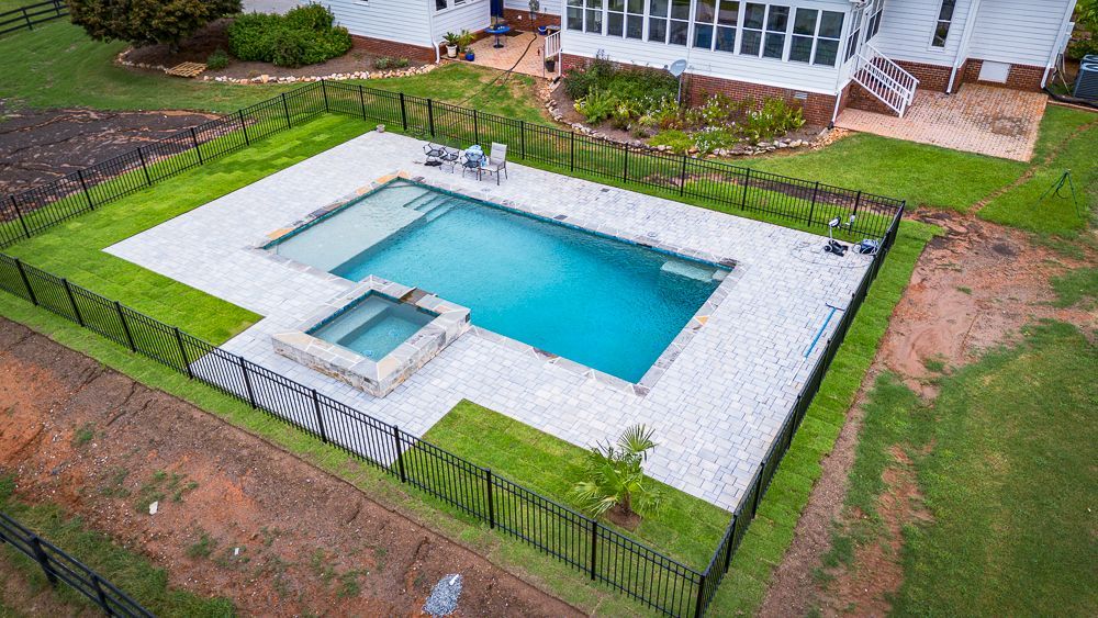 Aerial view of a backyard with a rectangular pool, hot tub, and black fence.