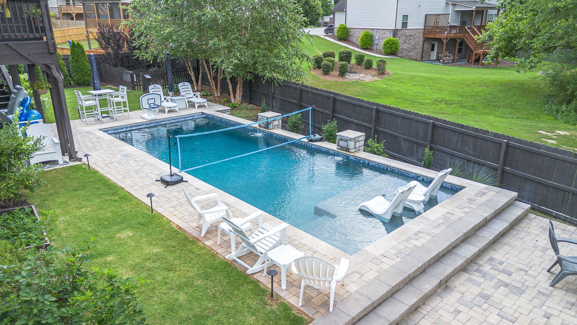Rectangular swimming pool surrounded by patio furniture in a backyard.
