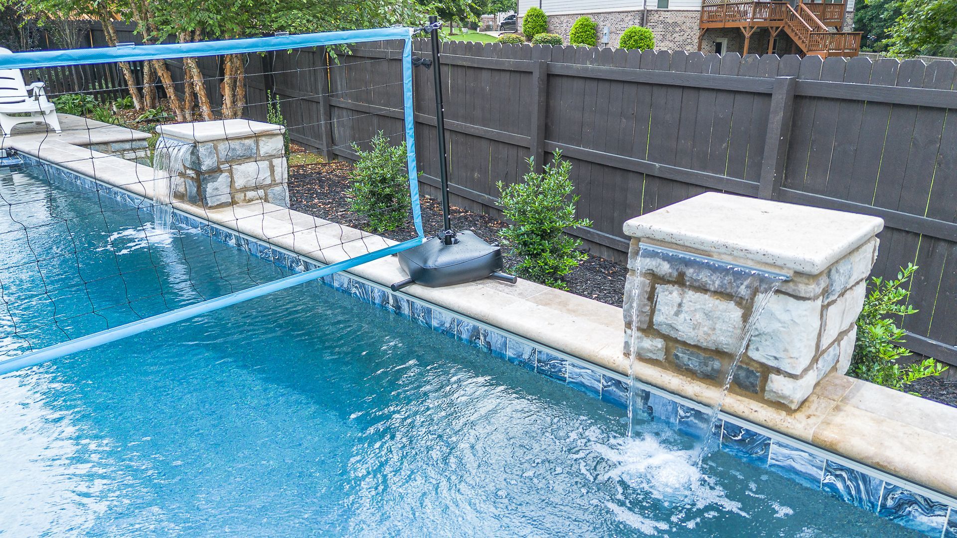 Pool with blue water, fountains, and stone pillars. A black fence in the background.